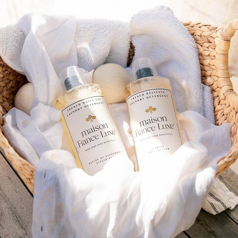 Natural Laundry detergents made in France, pictured in a laundry basket filled with linens and drier balls
